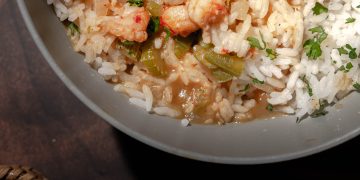 Bowl of steaming étouffée with shrimp and crawfish over white rice, garnished with green onions